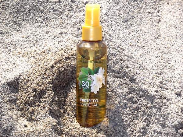 un flacon d'huile solaire en spray Yves Rocher dans le sable