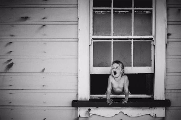 un enfant est penché à une fenêtre et crie sur cette photo en noir et blanc