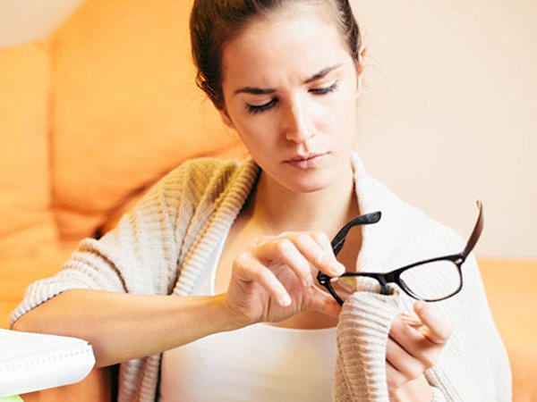 Femme qui nettoie ses lunettes avec sa chemise.