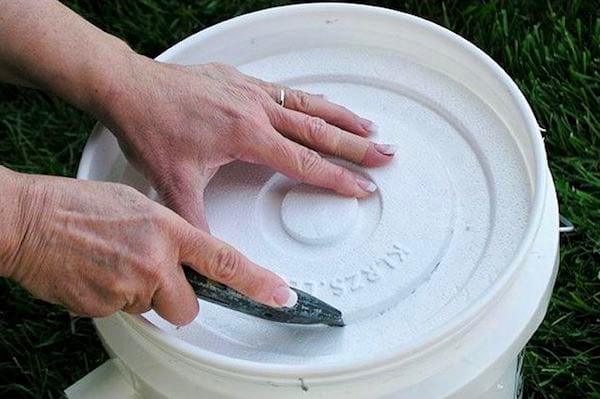 Des mains qui découpent un couvercle de seau en polystyrène pour faire une climatisation maison.