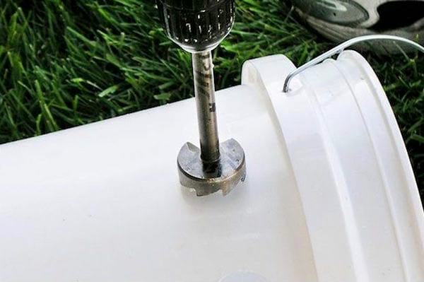 Une perceuse qui perce un trou dans un seau pour faire une climatisation maison.