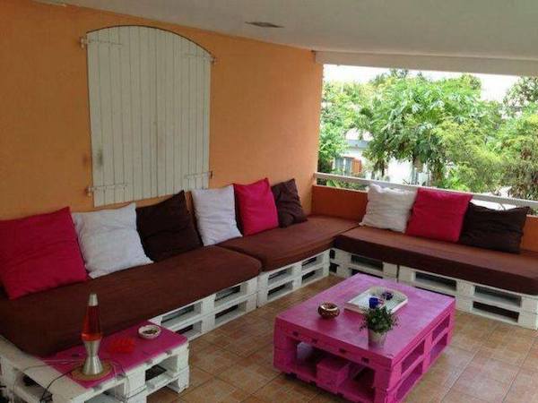 Long canapé et plusieurs coussins sur des palettes en bois blanc et une table basse avec des palettes en bois rose