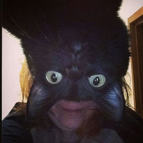 Une femme faisant un selfie avec la tête de son chat noir devant elle