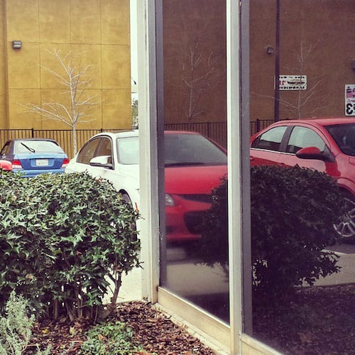 Plusieurs voitures garées sur un parking avec leurs reflets dans une vitre