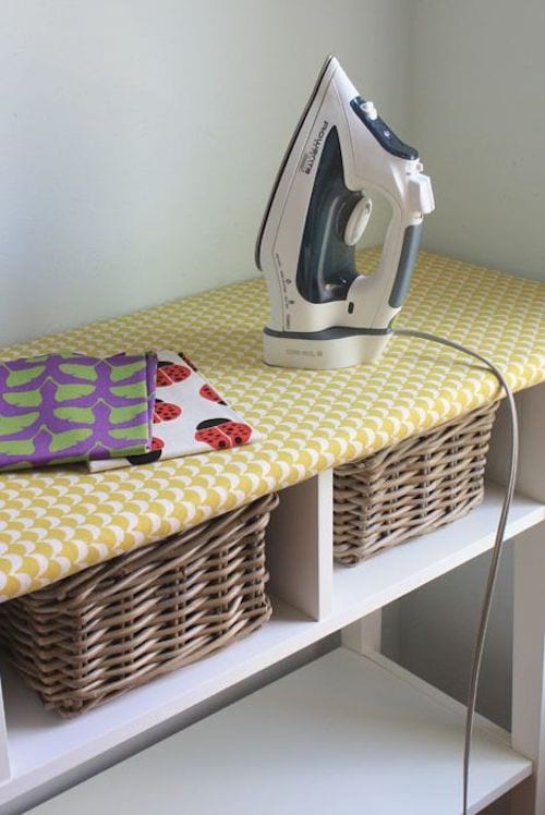 Table basique qui sert de repassage avec des paniers à linge en dessous 