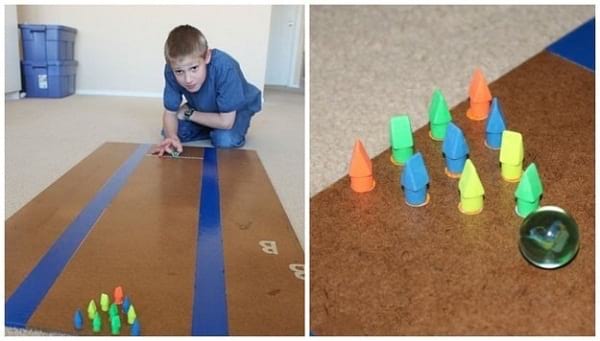 Un enfant joue à un bowling fait maison avec des gommes et une bille