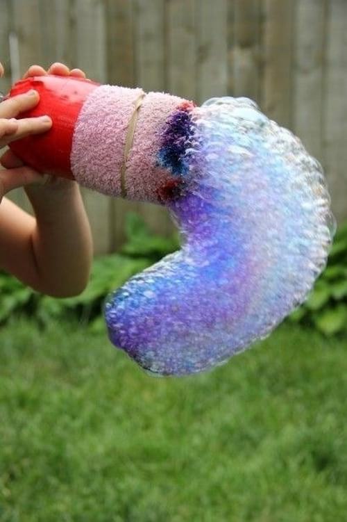 Un enfant souffle dans une bouteille pour faire un serpent de bulles multicolore