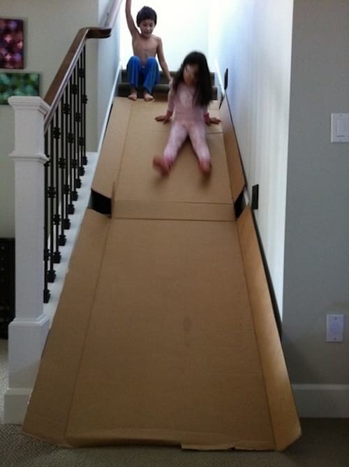 Deux enfant descendent sur un toboggan fait avec des cartons dans l'escalier