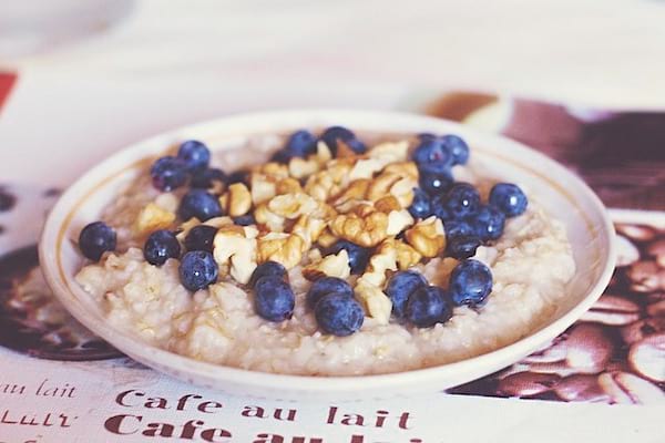 Une assiette avec du porridge cuit, des noix et quelques myrtilles par dessus sur un joural en français