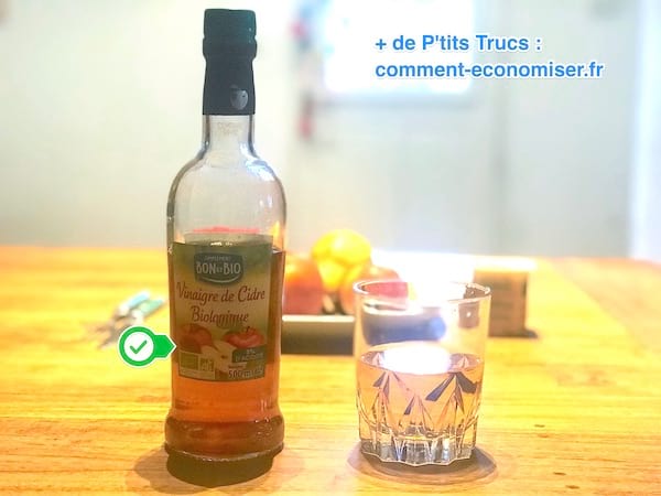 Eine Flasche Apfelessig mit einem halben Glas Essigwasser