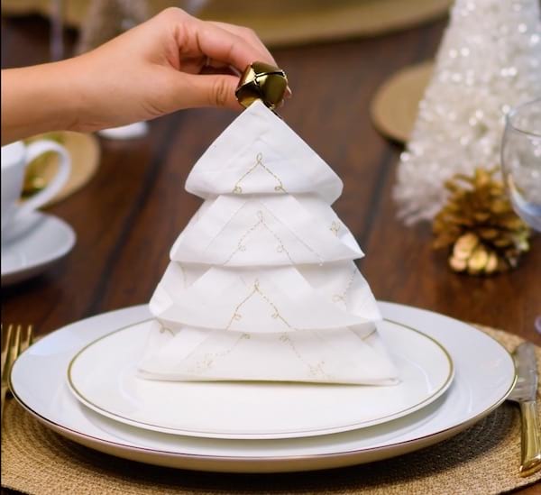 Guardanapo branco dobrado em uma árvore de Natal com um sino e colocado em um prato branco