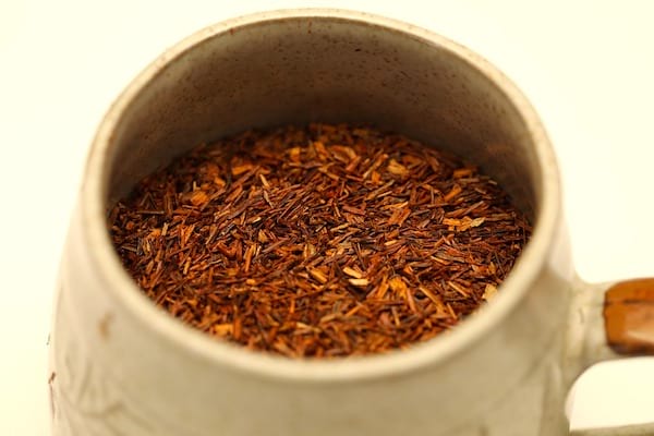 Un récipient rempli de thé rooibos, sur fond blanc.