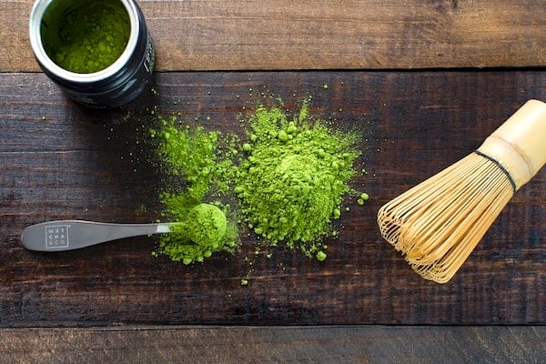 Du thé matcha et un fouet spécial à thé sur une table en bois.