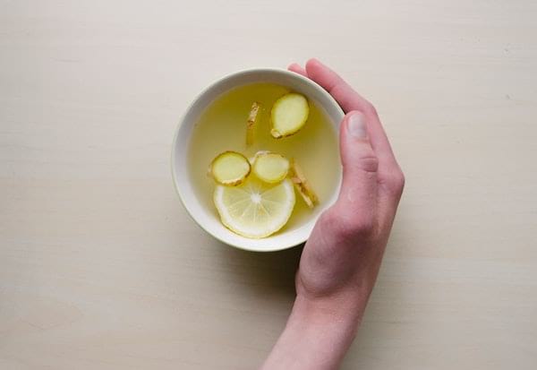 Main qui tient une tasse d'infusion de gingembre, sur fond blanc.