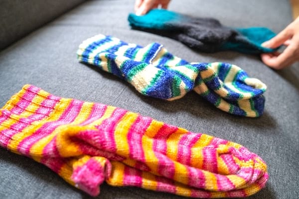 Des mains qui rangent des chaussettes dépareillées de différentes couleurs sur un canapé.