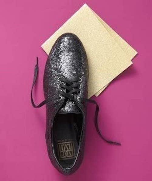 Une chaussure noire et du papier de verre, sur un fond colorié.