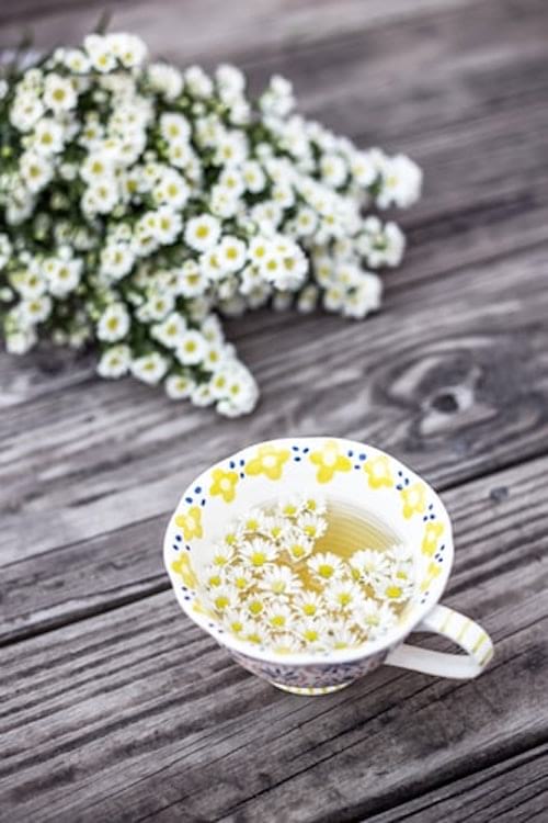 Une tasse de tisane de camomille avec des fleurs de camomille sur une table en bois.