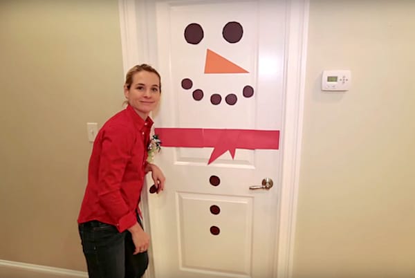 Une porte en forme de bonhomme de neige avec une femme habillée en rouge à côté