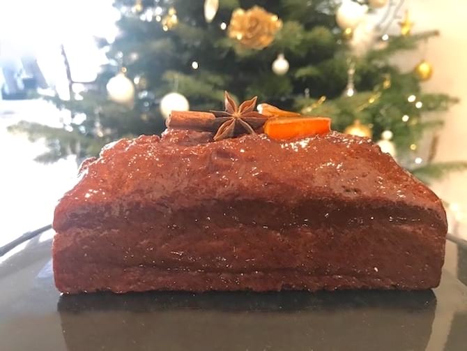 pain d'épices avec morceau d'orange et de cannelle devant un sapin de Noël