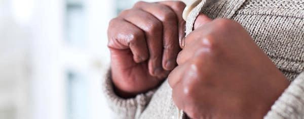 Des mains qui boutonnent un gilet en laine.