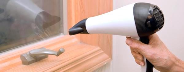 Une main qui applique un film thermique sur une fenêtre en bois avec un sèche-cheveux.