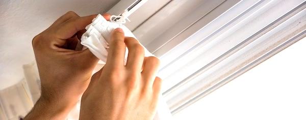 Des mains qui accrochent un rideau blanc.