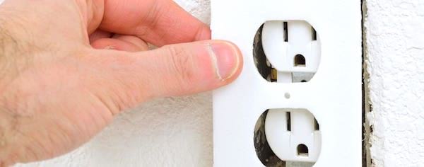 Une main qui enlève un cache de prise électrique.