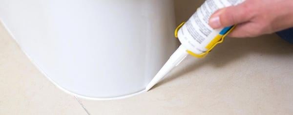 Des mains qui applique un joint silicon autour d'une canalisation blanche.