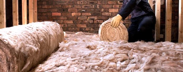 Un ouvrier qui déroule une isolation laine de verre dans des combles.