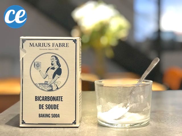 Un paquet de bicarbonate de soude posé sur une table en bois avec un verre et une cuillère 
