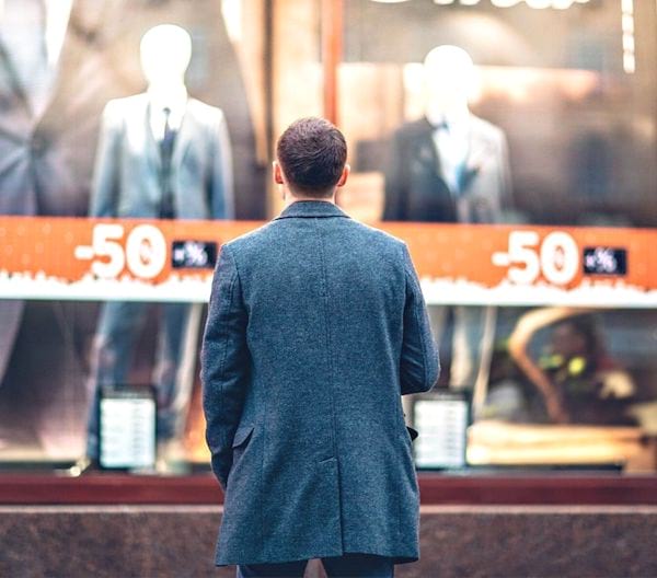 Un homme vu de dos devant une vitrine d'un magasin de vêtements.