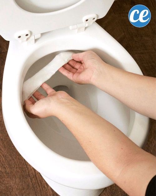 Des mains qui mettent du papier essuie-tout sous le rebord de la cuvette d'un WC.