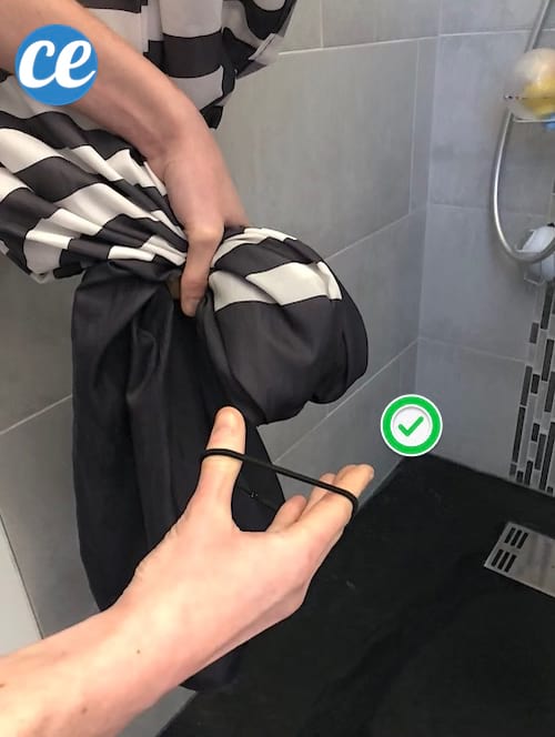 Une main qui accroche un élastique sur le rideau de douche pour éviter le moisi 