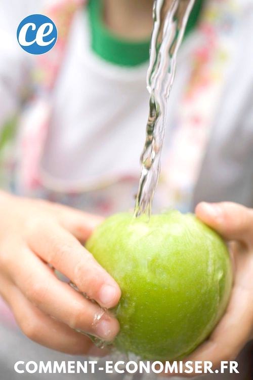 Des mains qui nettoient une pomme sous un filet d'eau.