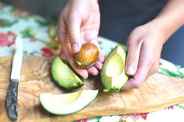 Noyau de l'avocat enlevé dans une main et trois quarts d'avocat sur la table
