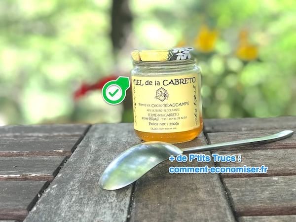Un pot de miel avec une cuillère posés sur une table en bois pour soigner le rhume des fois