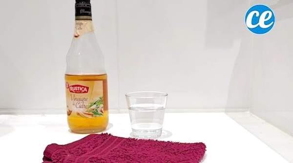 Une bouteille de vinaigre de cidre avec un verre d'eau et un gant pour faire un déodorant maison