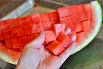 Une main qui tient une pastèque coupée en cubes.