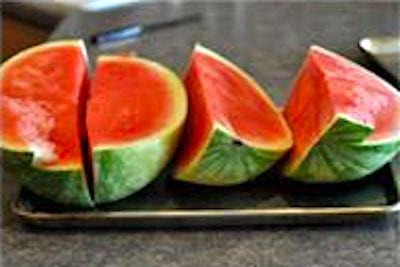 Une pastèque coupée en quartiers sur une plaque à pâtisserie avec rebords.