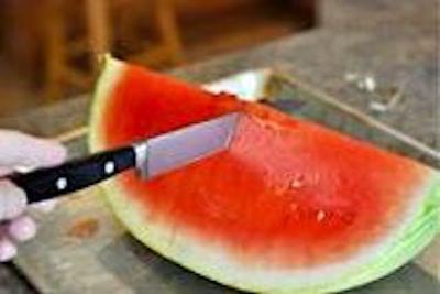 Un couteau qui coupe des tranches verticales de pastèque.