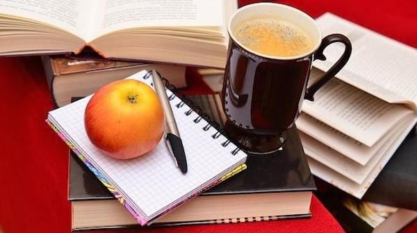 Une pomme, un café et des cahiers et des livres ouverts