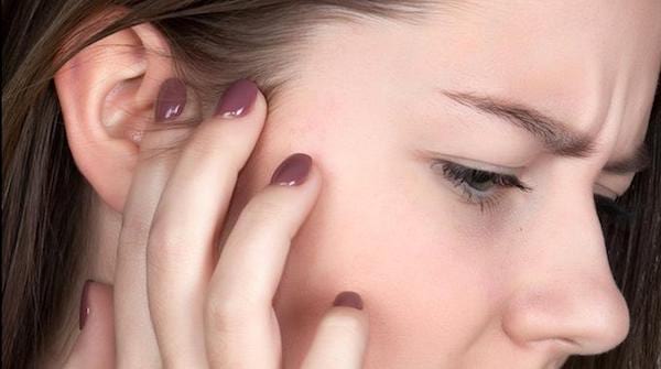 Une jeune femme se touche l'oreille à cause d'une douleur