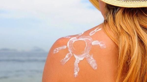 Une femme devant la mer avec un soleil dessiné sur l'épaule avec de crème solaire