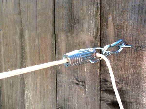 Un corde à linge en coton avec un tendeur en métal, devant une clôture en bois.
