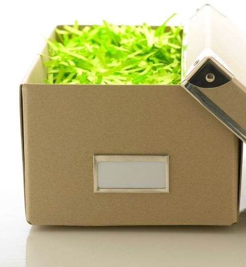Du papier jaune déchiqueté pour caler un cadeau dans une boîte sur fond blanc.