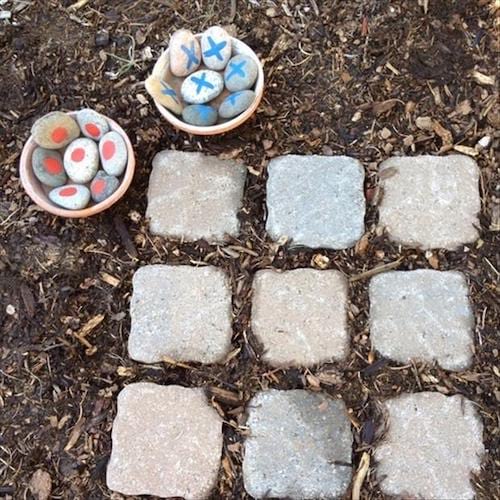 Un jeu du morpion fait avec des pierres et des pavés sur le sol en terre