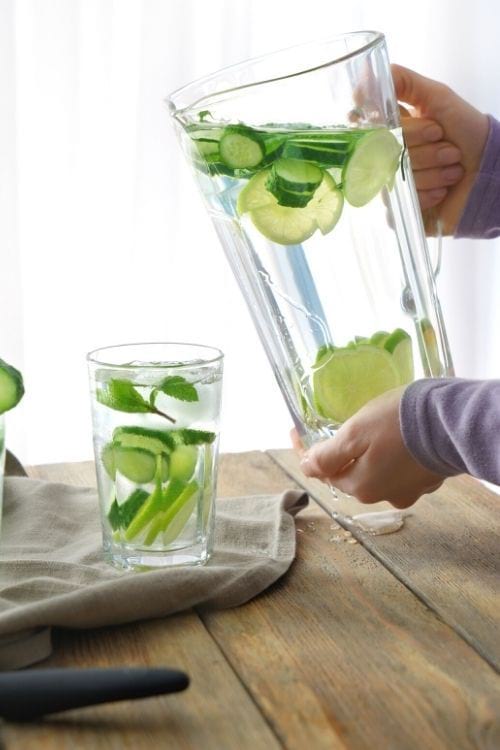 Des mains qui tiennent une cruche d'eau infusée au concombre.