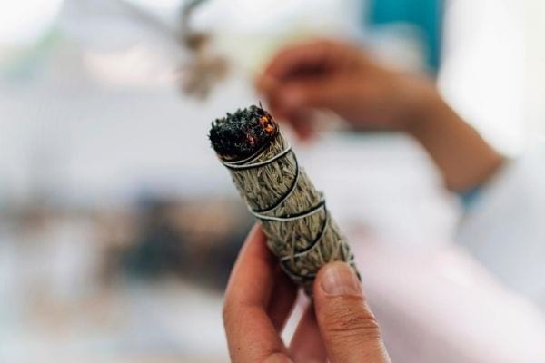 Une main qui tient un bâtonnet de sauge blanche qui brûle.