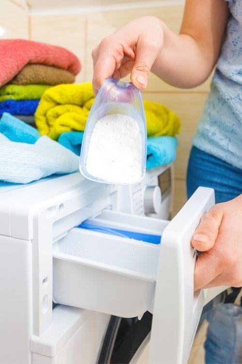 La mano de una mujer poniendo detergente en polvo en el cajón de detergente de una lavadora.