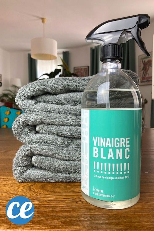 Une bouteille de vinaigre blanc devant une pile de serviettes éponge bien propres et moelleuses.